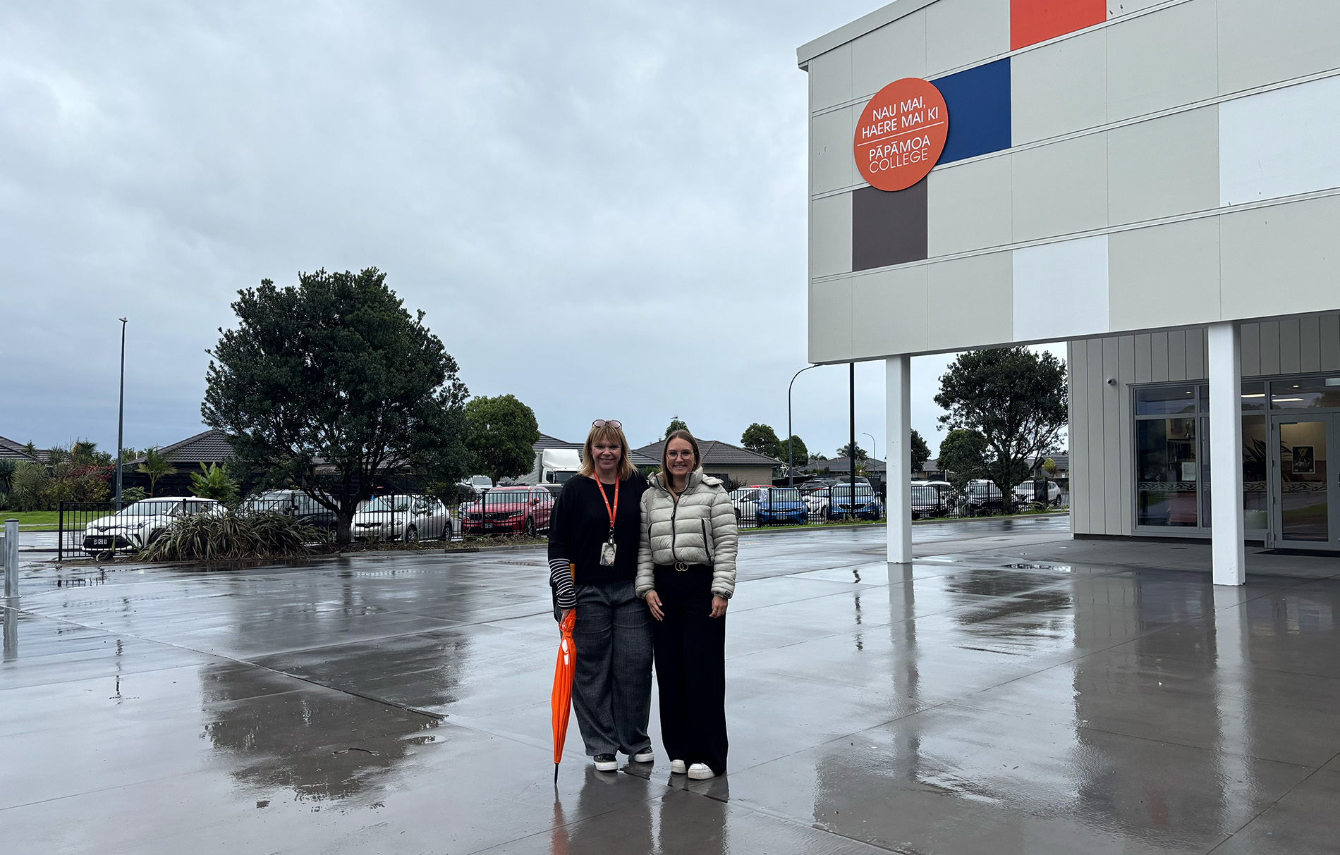 2 Frauen vor einer Schule bei grauem Regenwetter