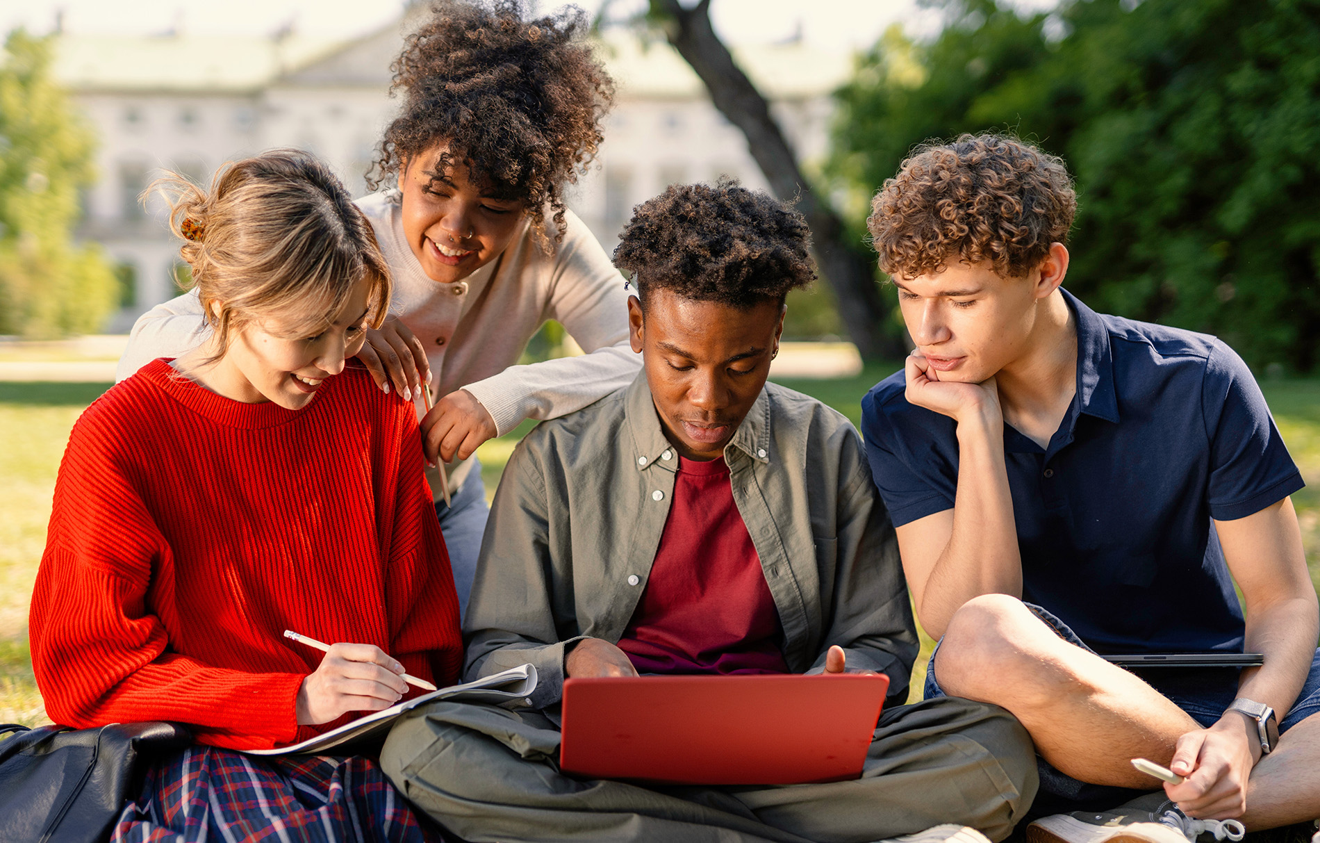 Gruppe Schüler sitzt vor einem Laptop im Park
