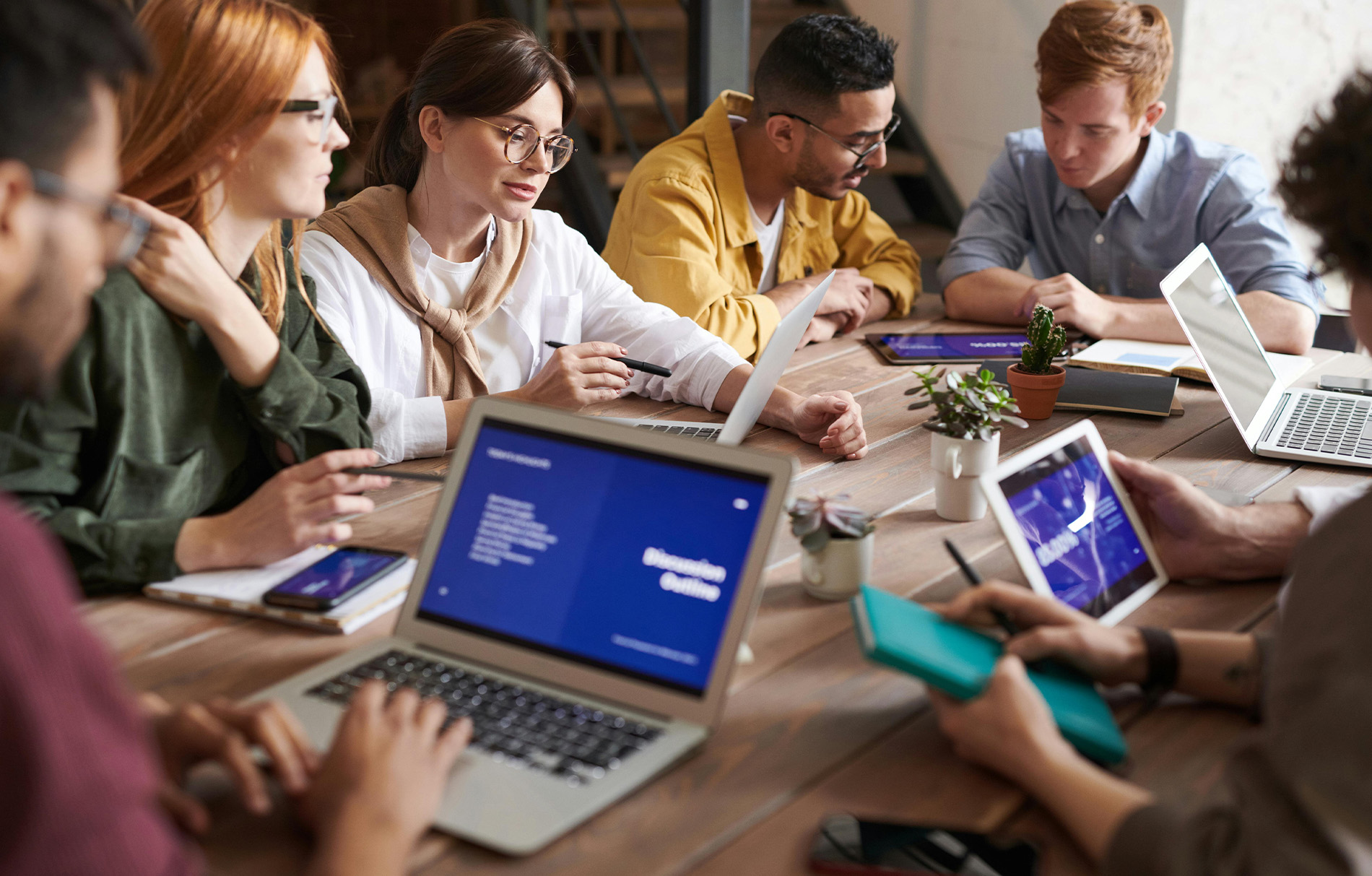 Personen sitzen um Tisch mit Laptops und Ipdas