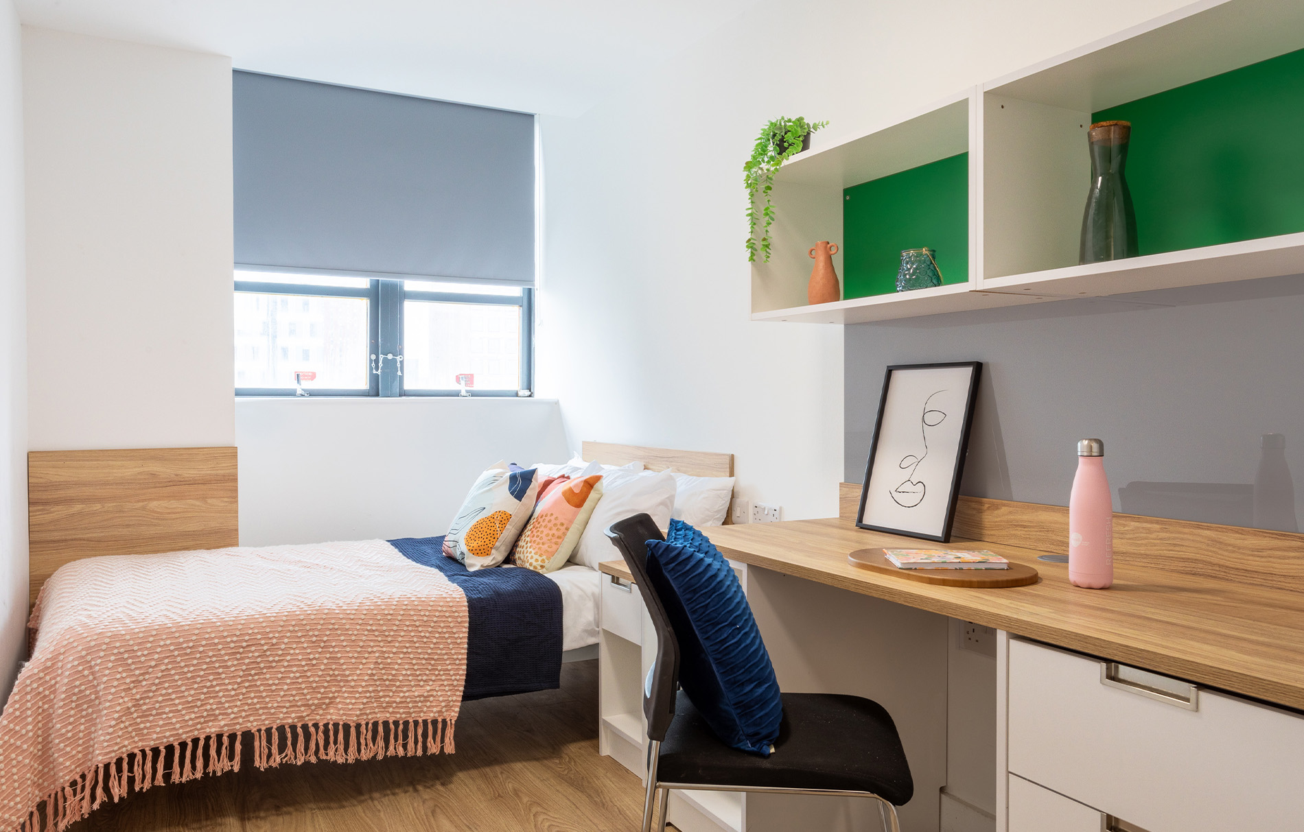 ein Zimmer mit einem Bett, auf dem eine bunte Decke liegt, einem Schreibtisch und einem bunten Regal