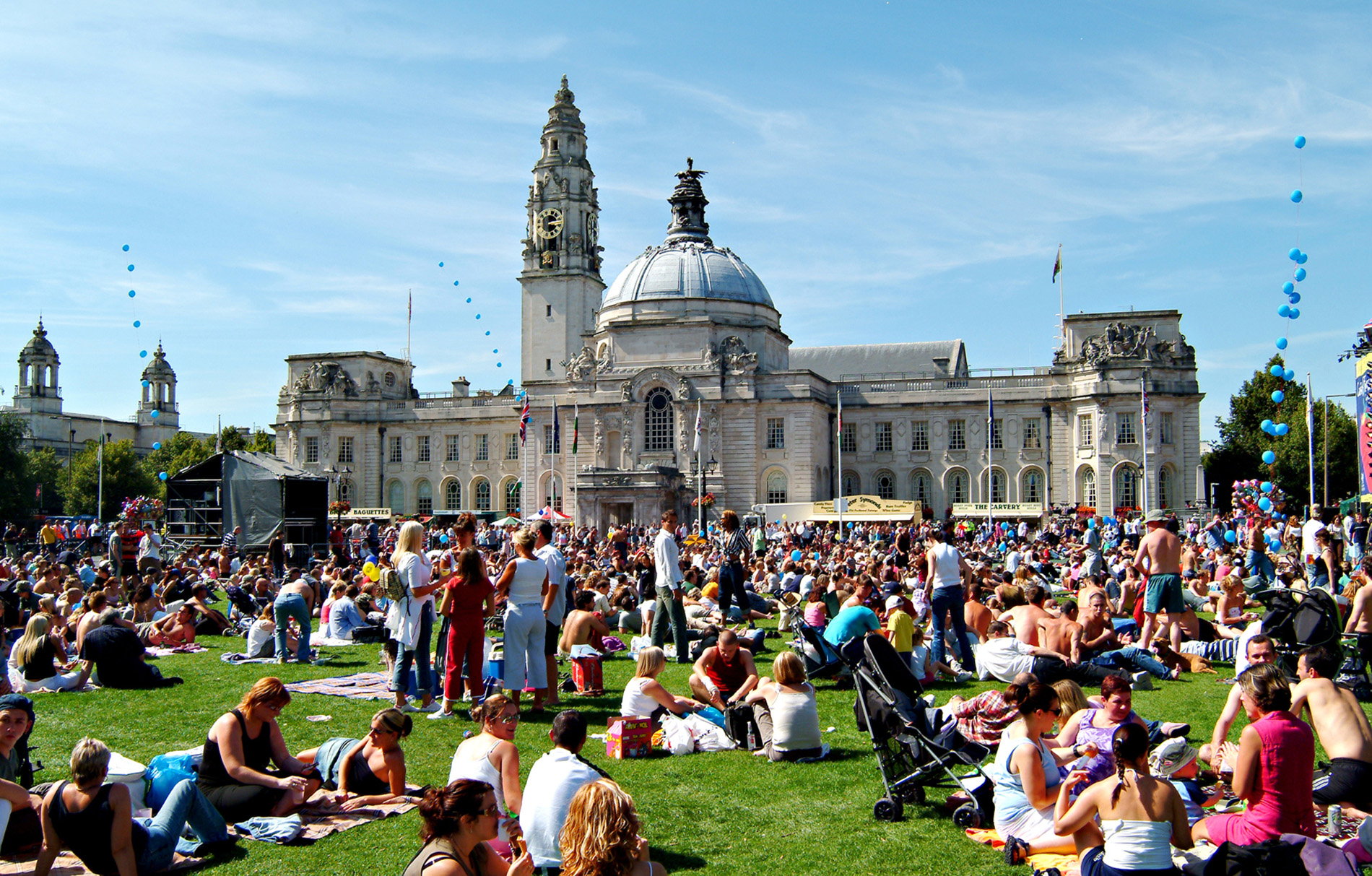 Menschen sitzen an einem sonnigen Tag auf der Rasenfläche vor dem Rathaus von Cardiff