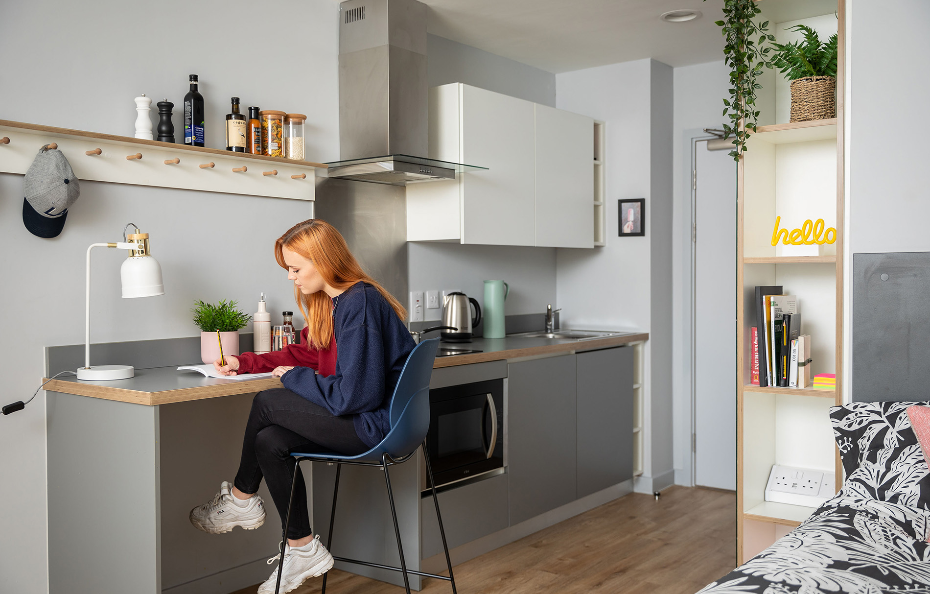einen modernen Raum mit Bett und Kochzeile, an der eine junge Frau sitzt