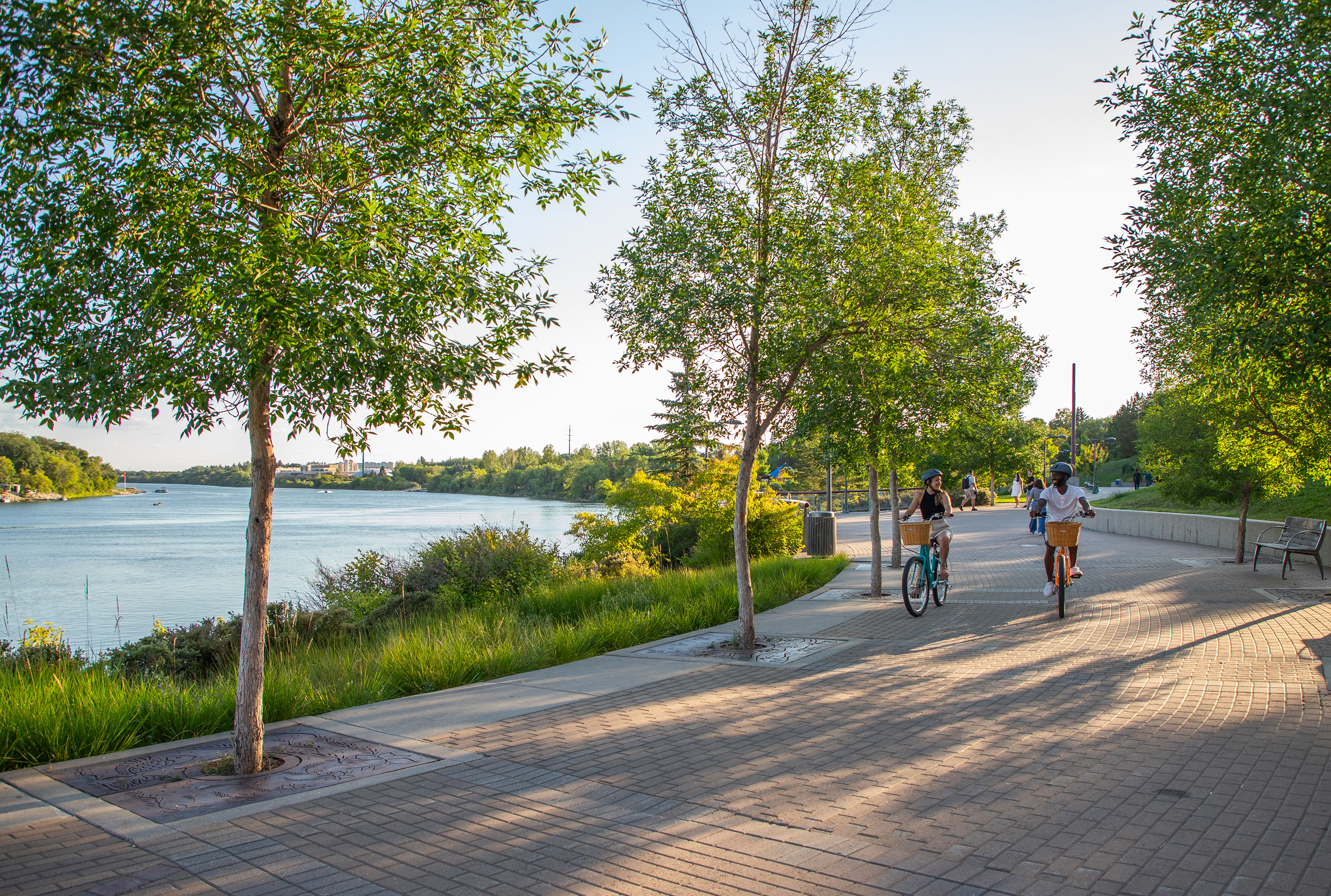 Promenade mit zwei Fahrradfahrern entlang eines Flusses.