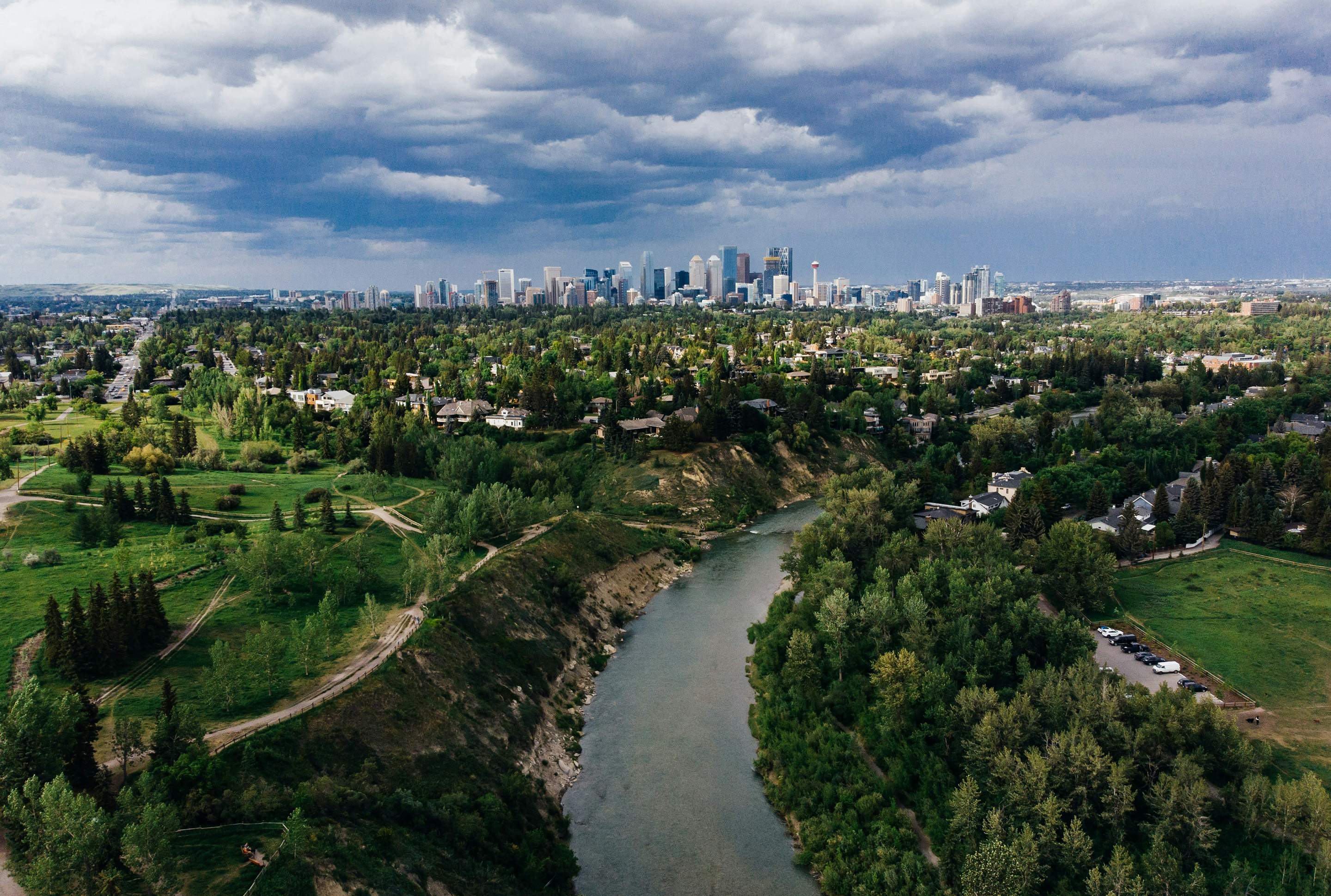 Grüner Wald mit Fluss im Vordergrund, in der Ferne die Skyline einer kanadischen Stadt