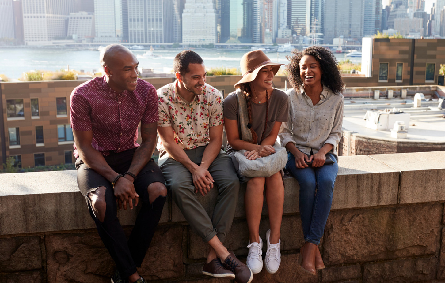 Freunde sitzen auf einer Mauer, im Hintergrund ist die Skyline von New York
